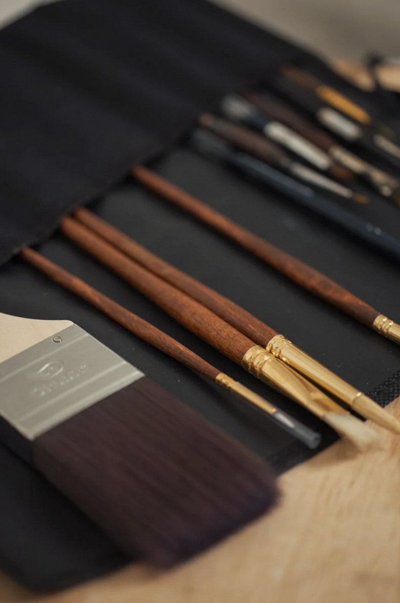 Close-up of various paintbrushes in a fabric holder, essential for artists.